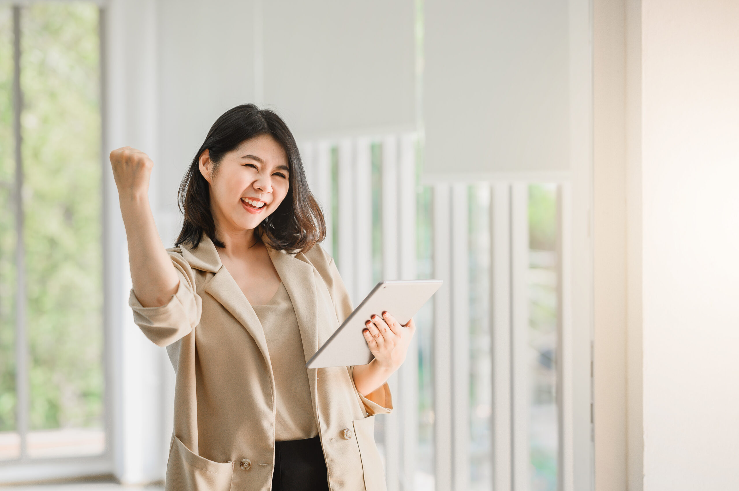 Asian woman holding digital tablet and raising her arm up